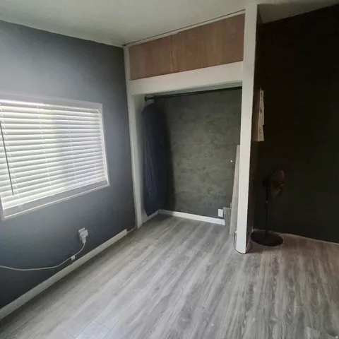 Room featuring wood-finish flooring, a window with horizontal blinds, and a built-in closet with a hanging rod
