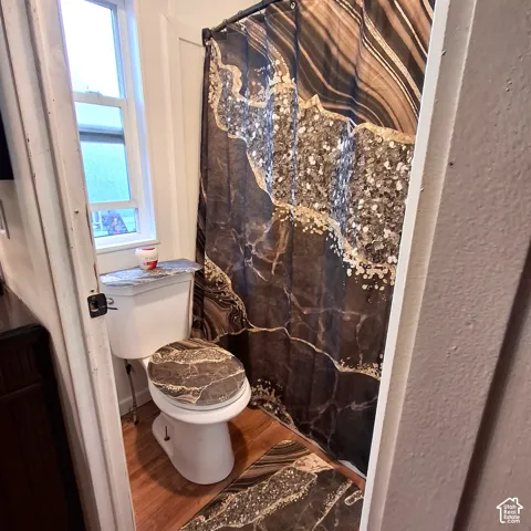 Bathroom featuring a white toilet, wood-finish flooring, and a single window