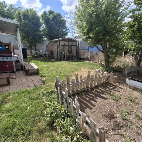 Expansive backyard featuring a patio with paver stones, a lawn area, a storage shed, a garden bed with a picket fence, and mature trees