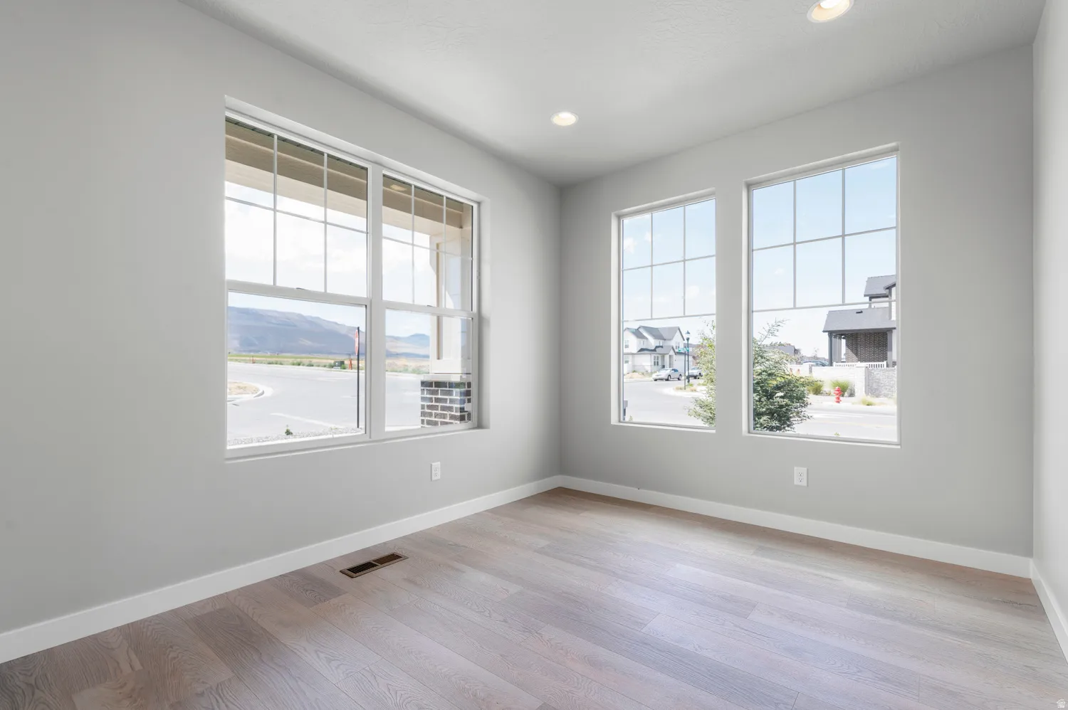 Spacious room featuring multiple large windows with grid patterns, light wood-finish flooring, recessed lighting, and crisp white trim