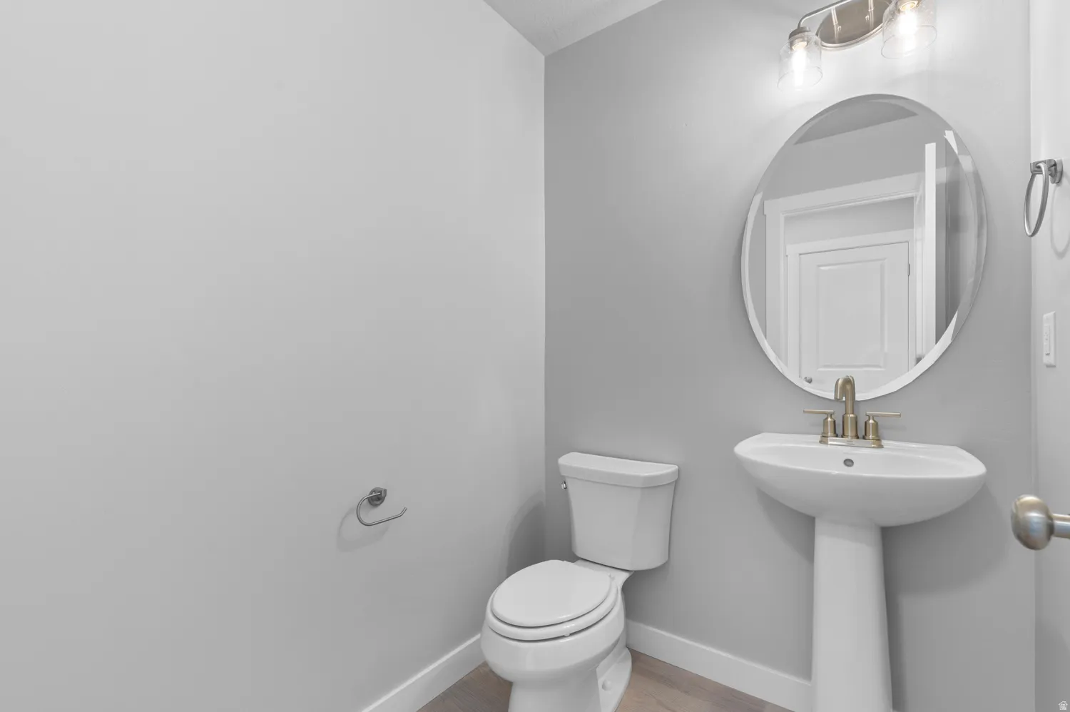 Powder room featuring a pedestal sink, oval mirror, and wall-mounted light fixture