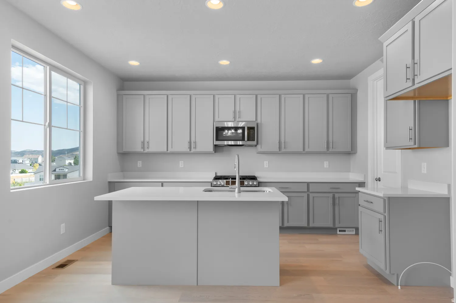 Kitchen featuring a central island with an integrated sink, light wood-finish flooring, recessed lighting, stainless steel appliances, and ample cabinetry with light countertops