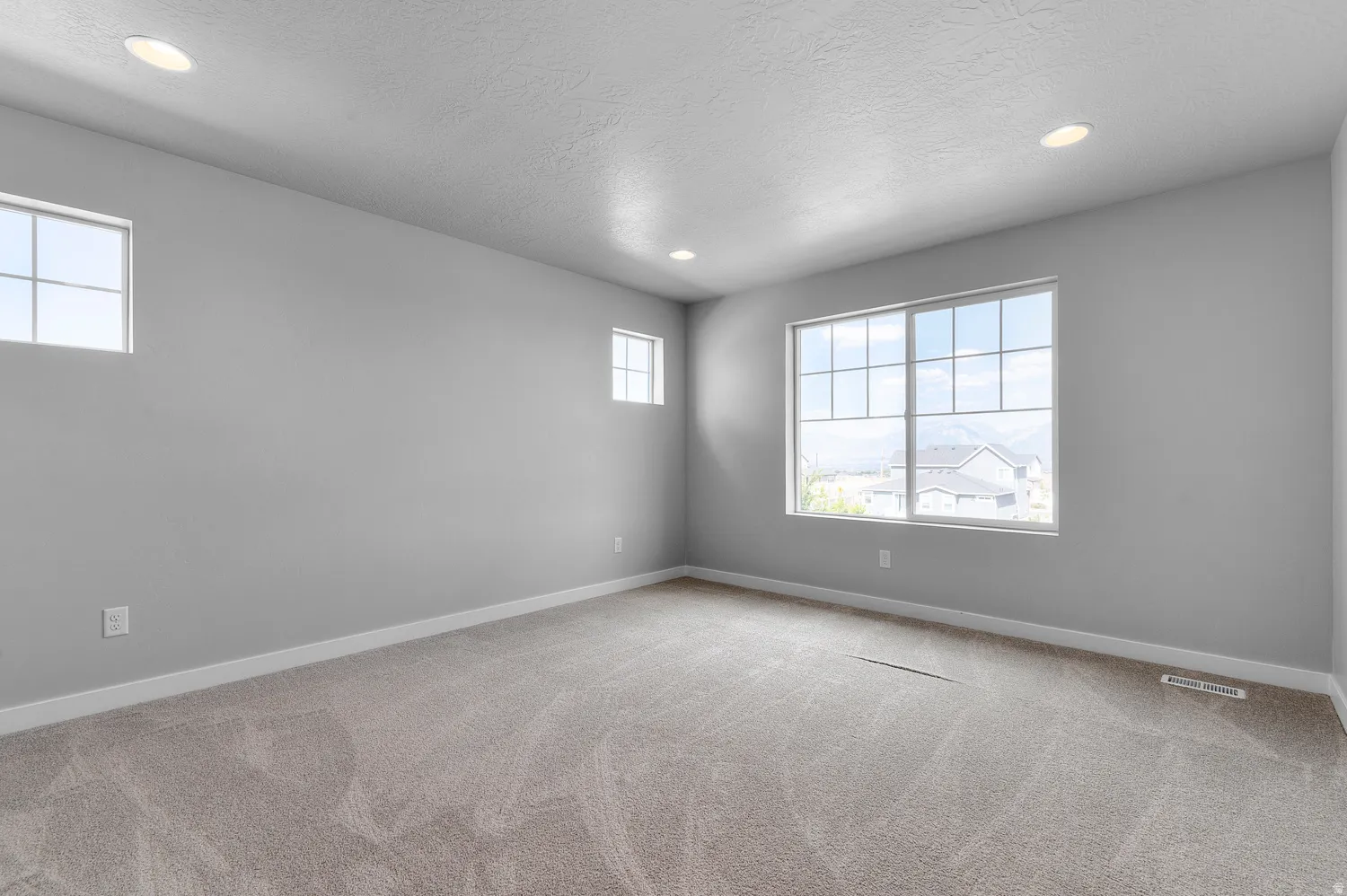 Spacious room with plush carpet flooring, recessed lighting, and multiple windows providing ambient illumination