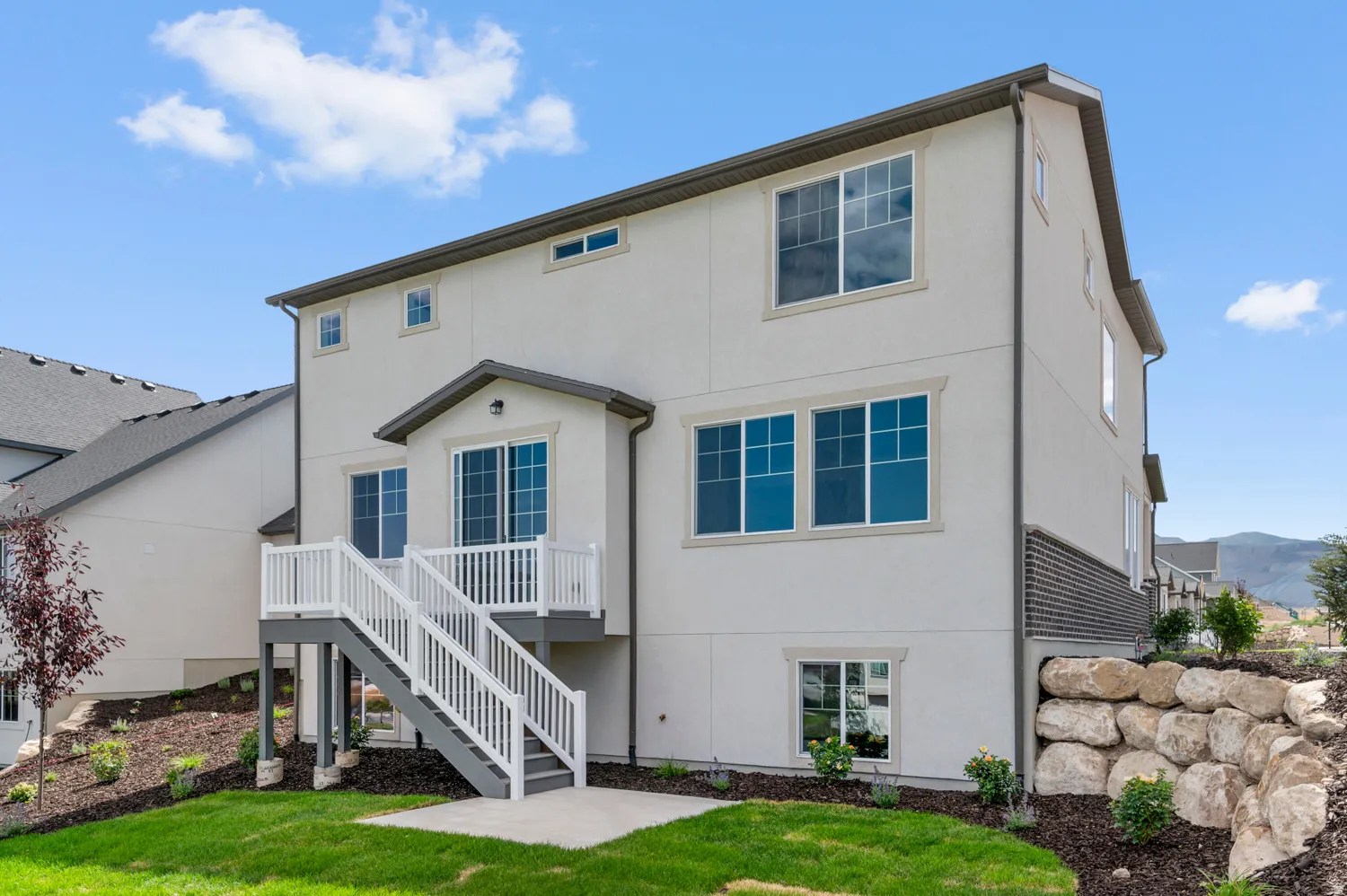 Rear elevation featuring a stucco exterior, multi-level windows, a second-story deck with white railings, and a concrete patio