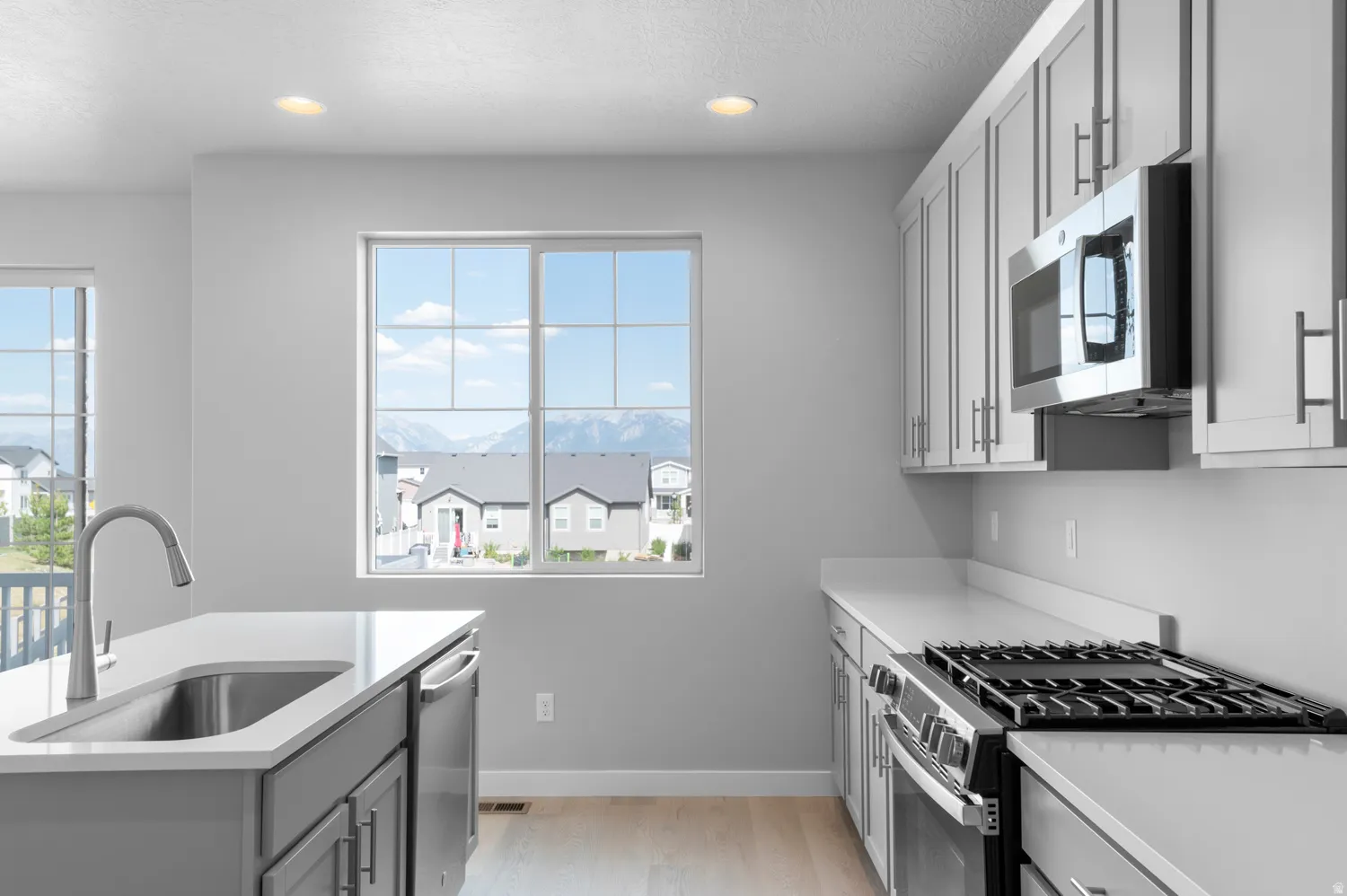 Modern kitchen featuring light gray cabinetry, stainless steel appliances, a center island with an undermount sink, and recessed lighting