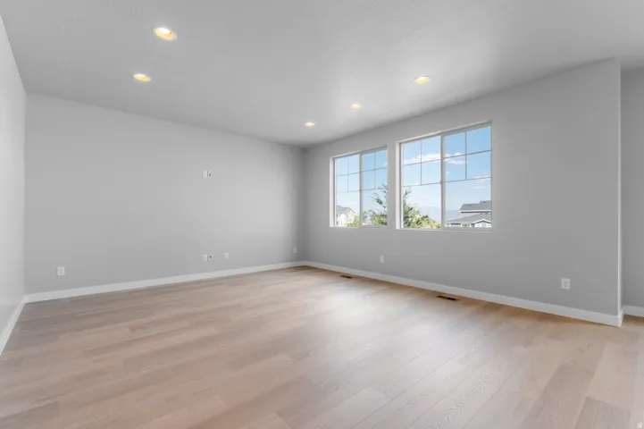 Spacious interior room featuring light-toned wood-finish flooring, recessed lighting, and two large windows with grid patterns