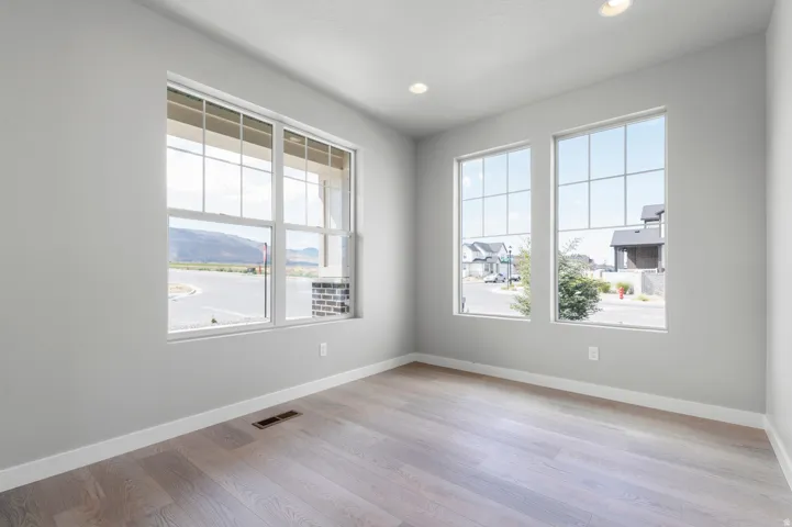 Spacious room featuring multiple large windows with grid patterns, light wood-finish flooring, recessed lighting, and crisp white trim