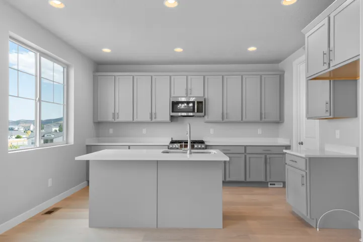 Kitchen featuring a central island with an integrated sink, light wood-finish flooring, recessed lighting, stainless steel appliances, and ample cabinetry with light countertops