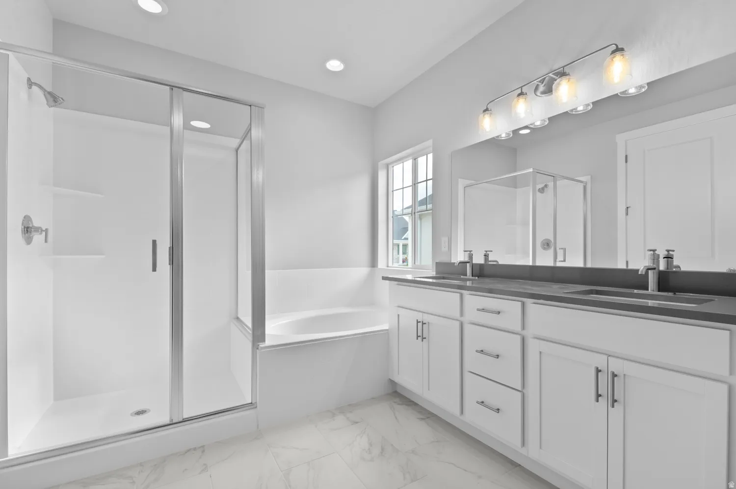 Spacious bathroom featuring a double vanity with stone countertops, a large framed mirror, and a five-light fixture