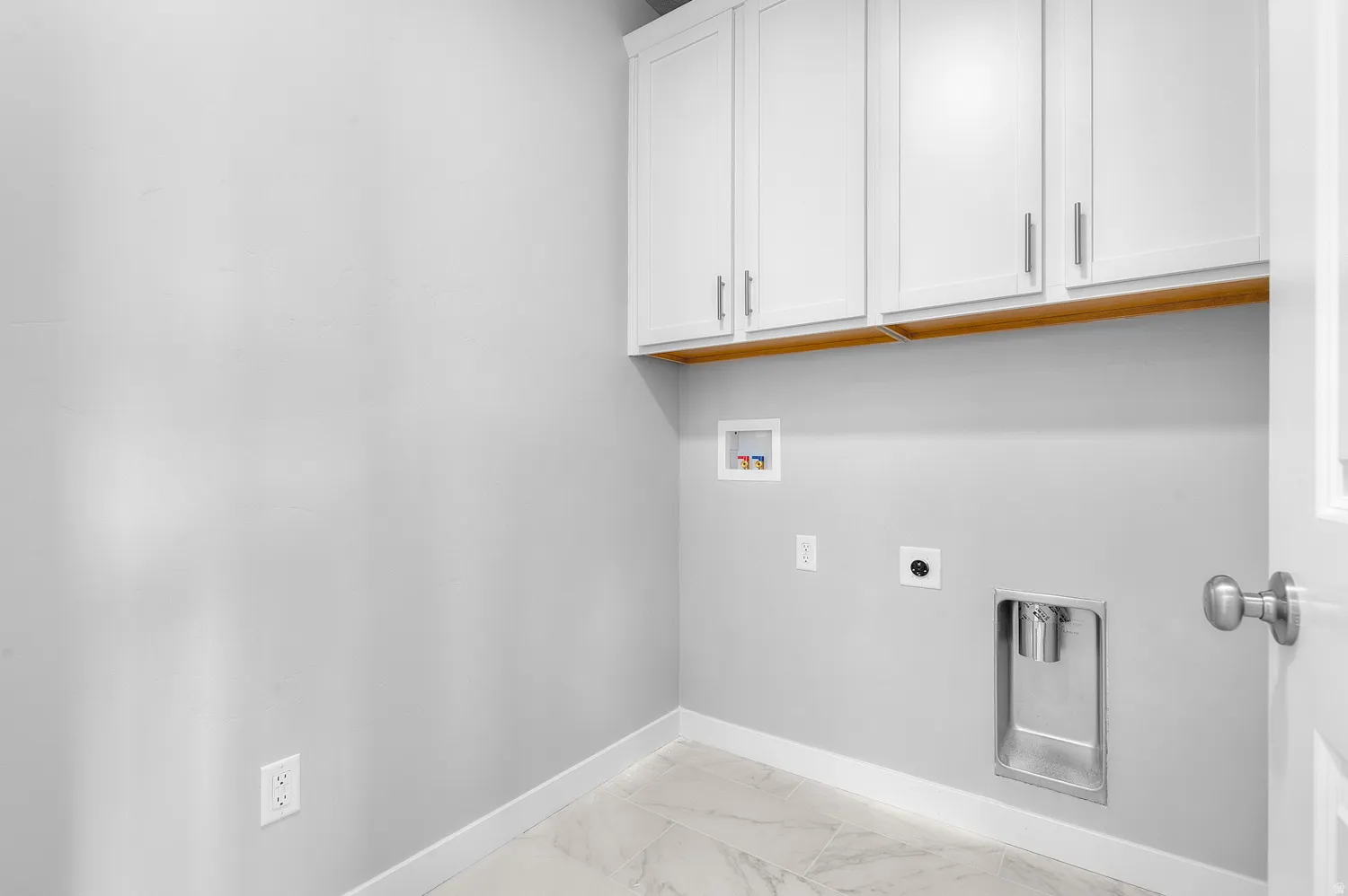 Utility area featuring white shaker-style cabinetry with chrome hardware, a wood-finish shelf, and light-toned tile flooring