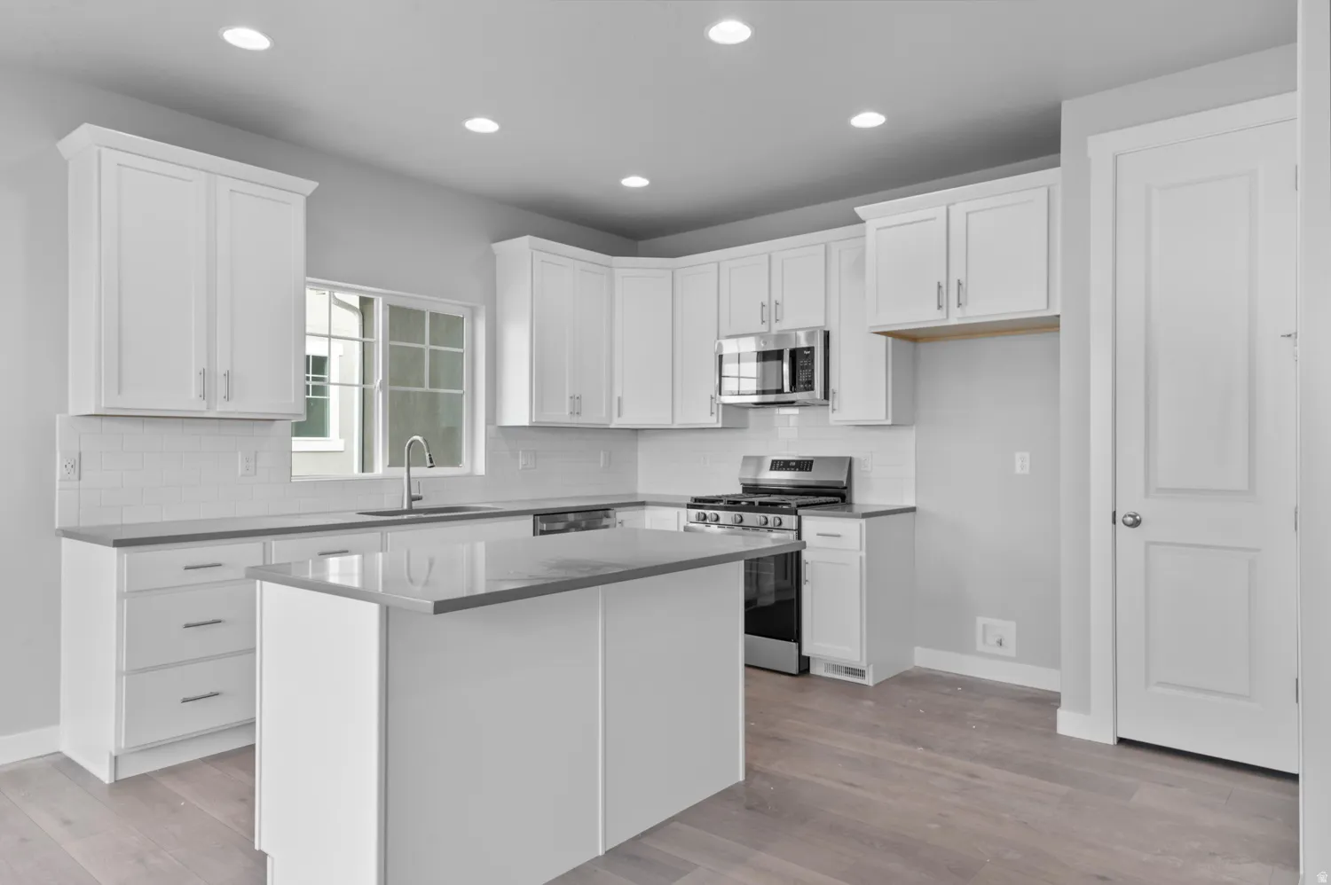 Modern kitchen featuring white shaker cabinetry, stainless steel appliances, a center island with countertop seating, recessed lighting, and wood-finish flooring