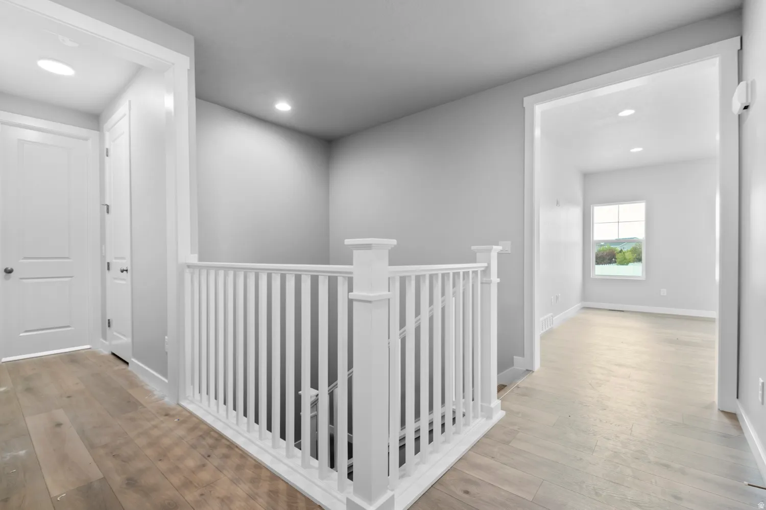Upper level landing featuring light wood-finish flooring, white spindle railing, recessed lighting, and crisp white trim