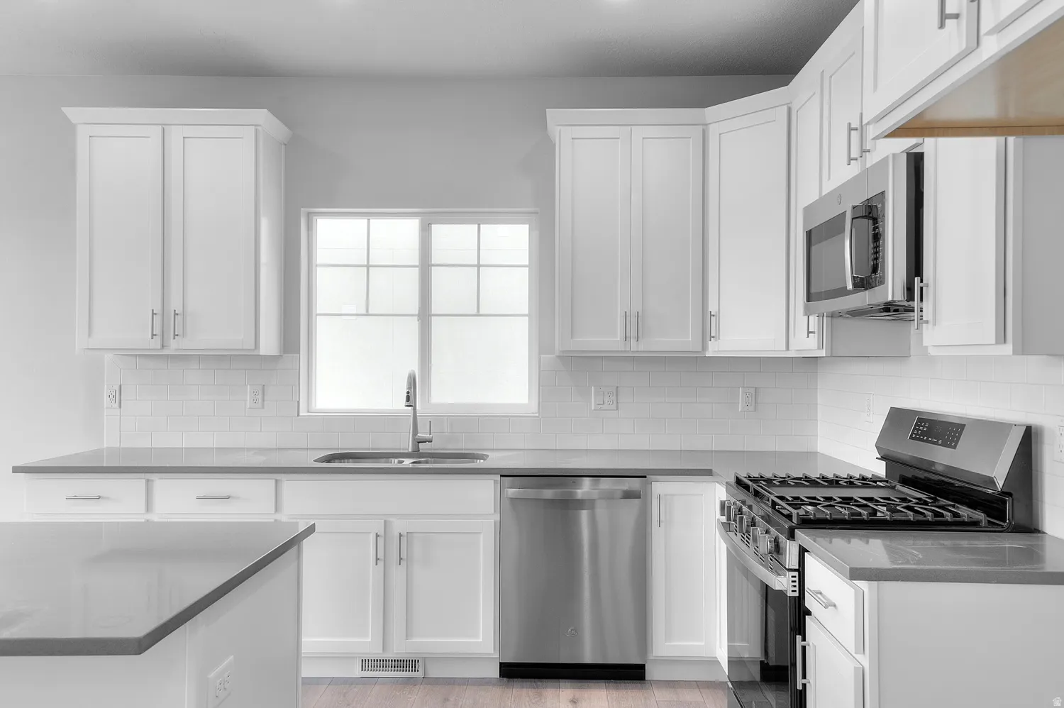 Kitchen featuring white shaker cabinetry, stainless steel appliances, light gray countertops, white subway tile backsplash, and wood-finish flooring