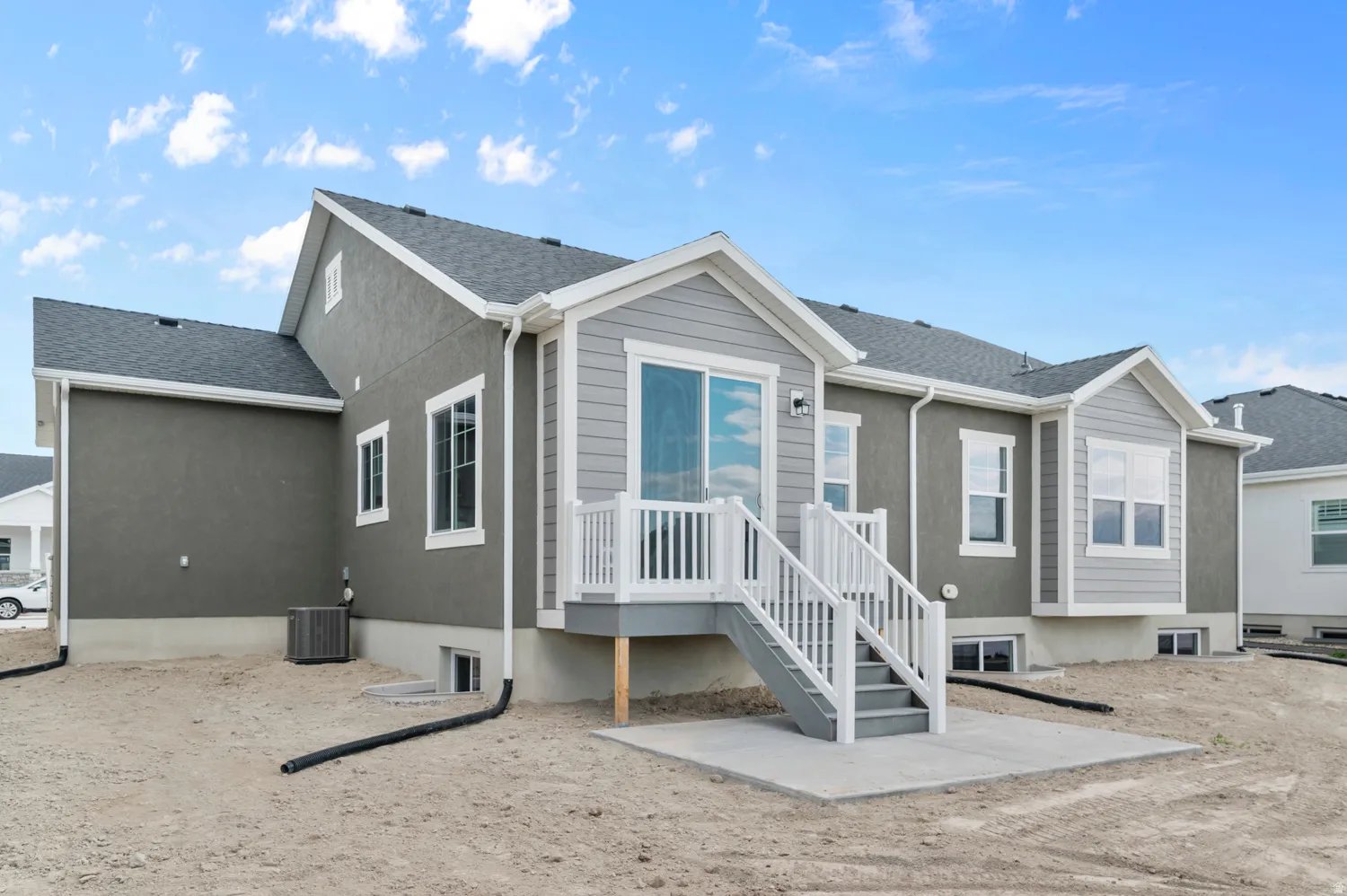 Rear exterior featuring a sliding glass door, private deck with white railing, and a concrete patio