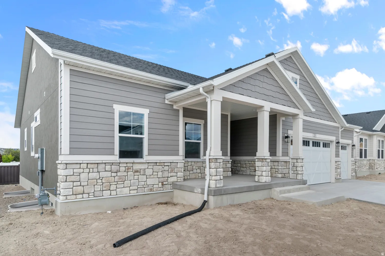 Gray siding exterior with a stone veneer foundation, covered front porch, and white garage door