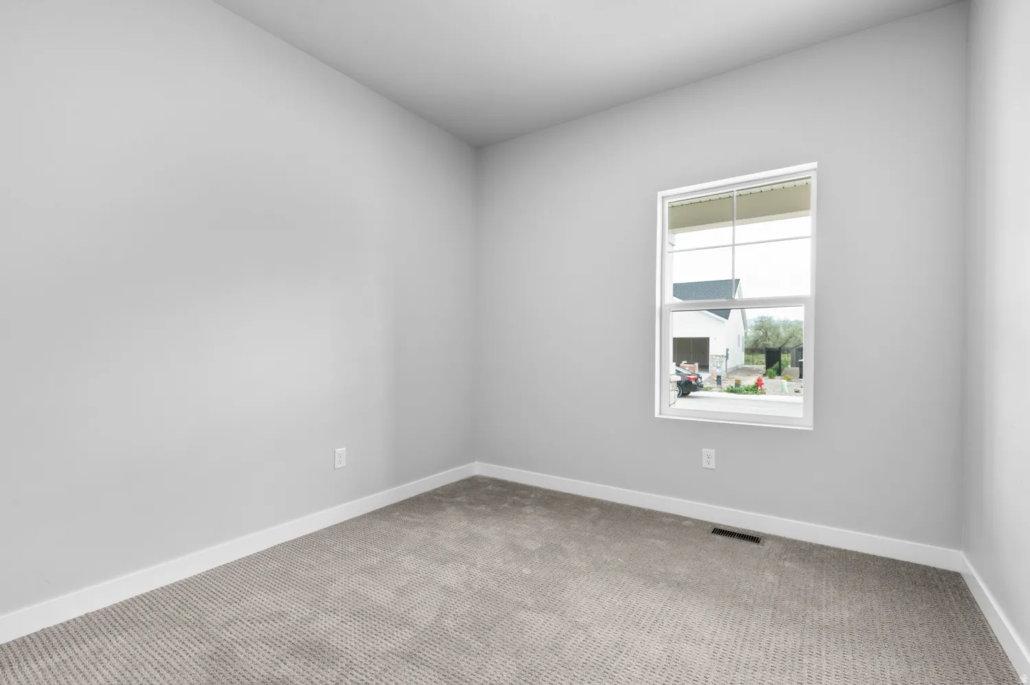 Neutral-toned walls and plush gray carpeting characterize this room, featuring a white-framed window