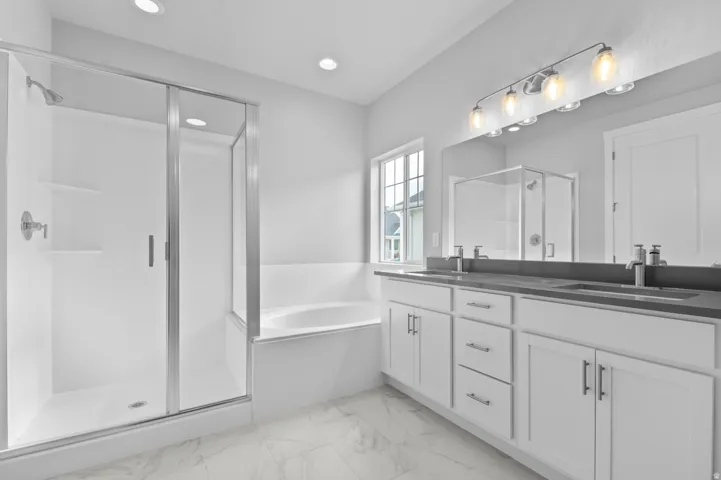 Spacious bathroom featuring a double vanity with stone countertops, a large framed mirror, and a five-light fixture