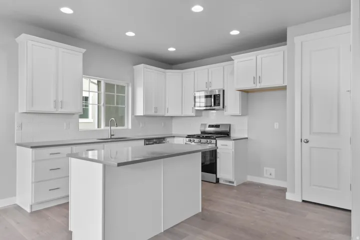 Modern kitchen featuring white shaker cabinetry, stainless steel appliances, a center island with countertop seating, recessed lighting, and wood-finish flooring
