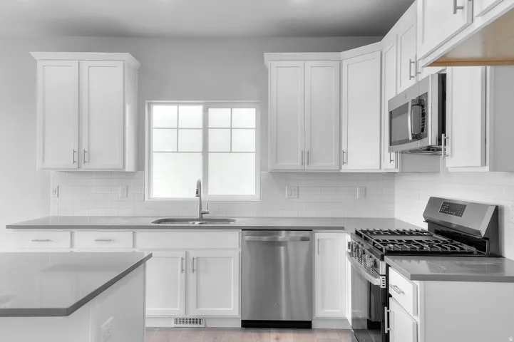 Kitchen featuring white shaker cabinetry, stainless steel appliances, light gray countertops, white subway tile backsplash, and wood-finish flooring