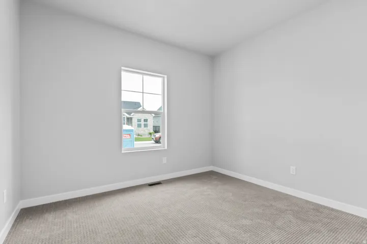 Carpeted room featuring a white-framed window, light gray walls, and white baseboards