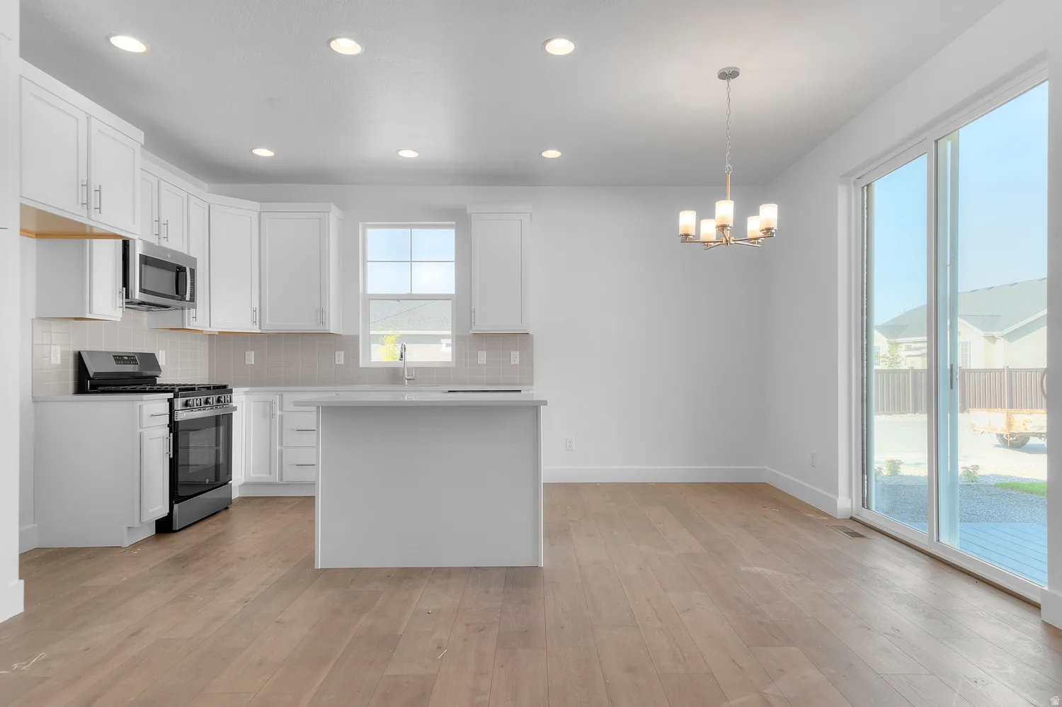 Open-concept kitchen featuring white shaker cabinetry, stainless steel appliances, a center island with countertop seating, and wood-finish flooring
