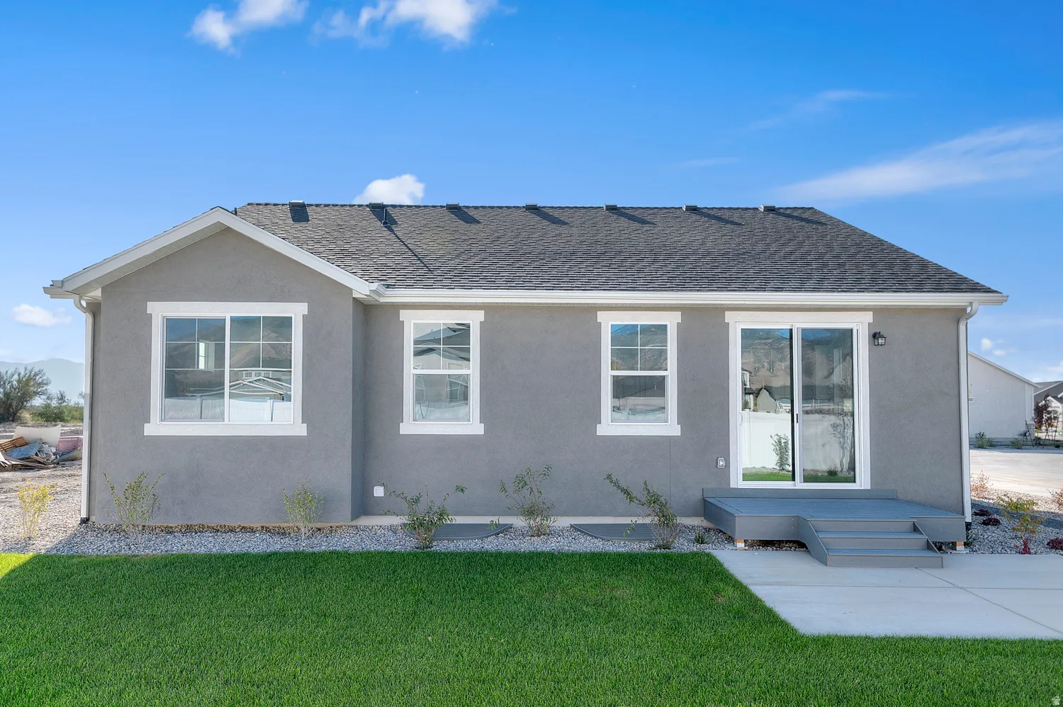 Rear exterior featuring a gray stucco finish and a dark shingle roof