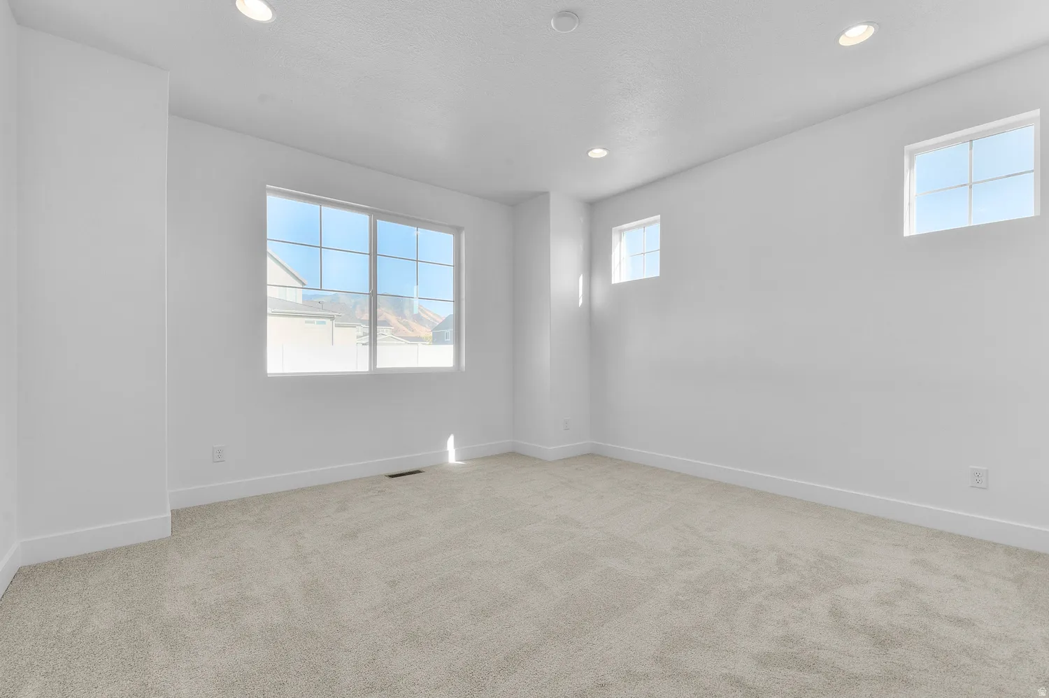 Spacious room featuring light-toned carpeting, white walls, and recessed lighting