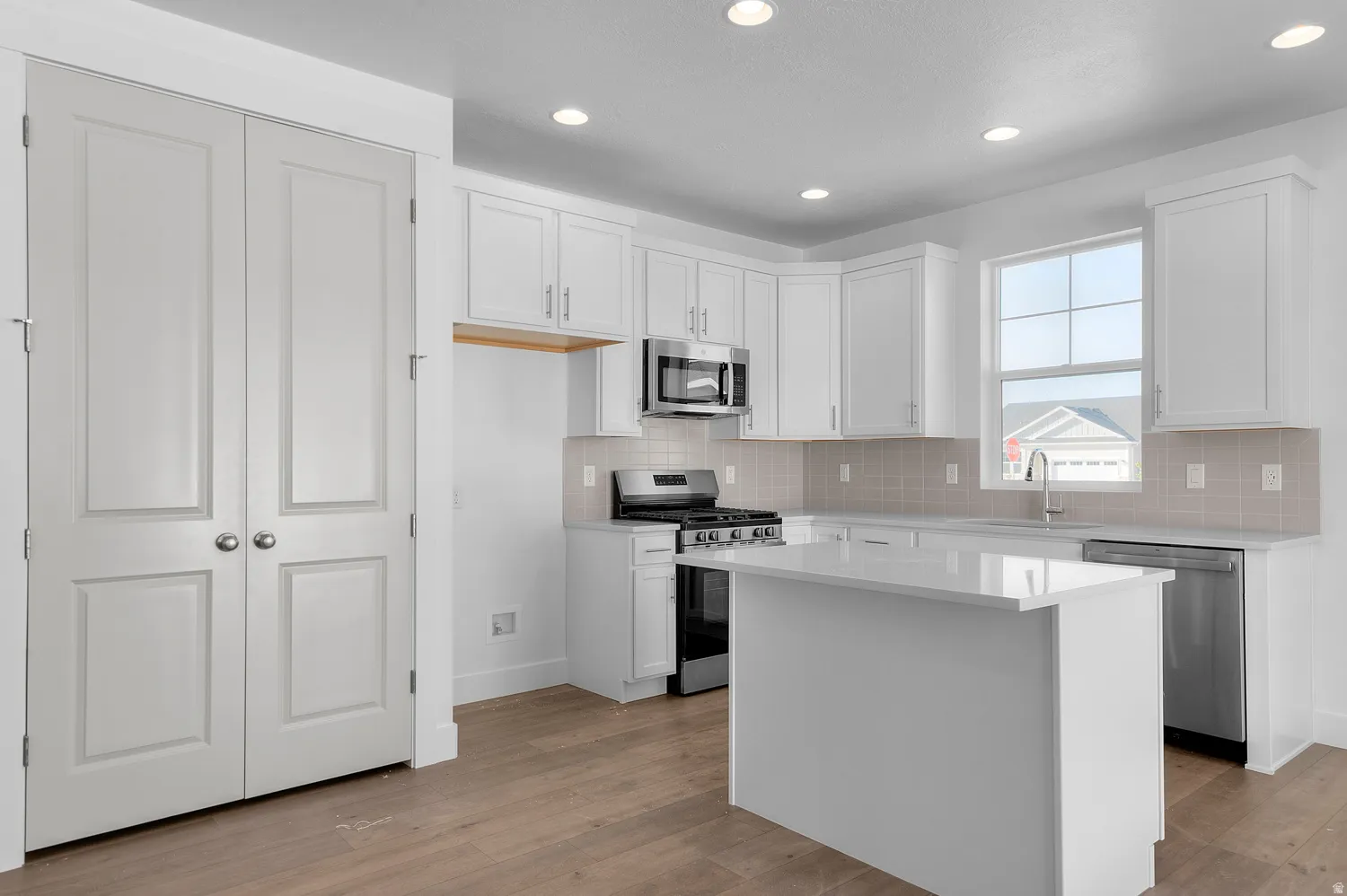 Modern kitchen featuring white cabinetry, a central island with a solid surface countertop, stainless steel appliances, and wood-finish flooring