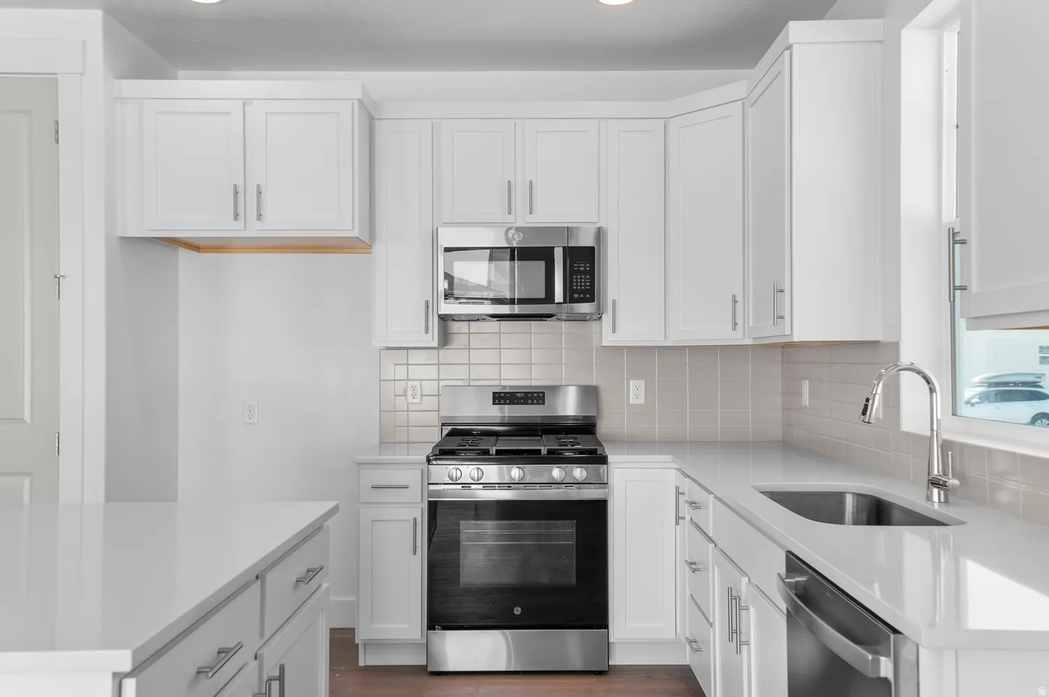 Modern kitchen featuring white shaker cabinetry, stainless steel appliances, a subway tile backsplash, and light-toned countertops