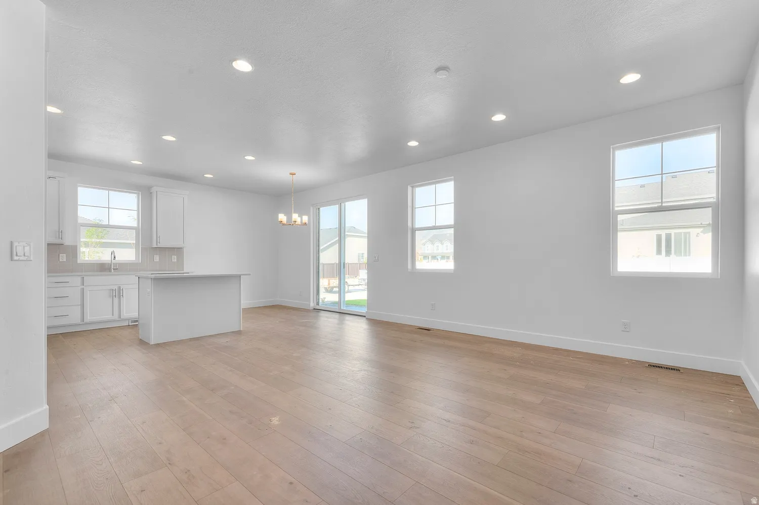 Open-concept living space featuring wood-finish flooring, recessed lighting, and ample natural light from multiple windows and a sliding glass door