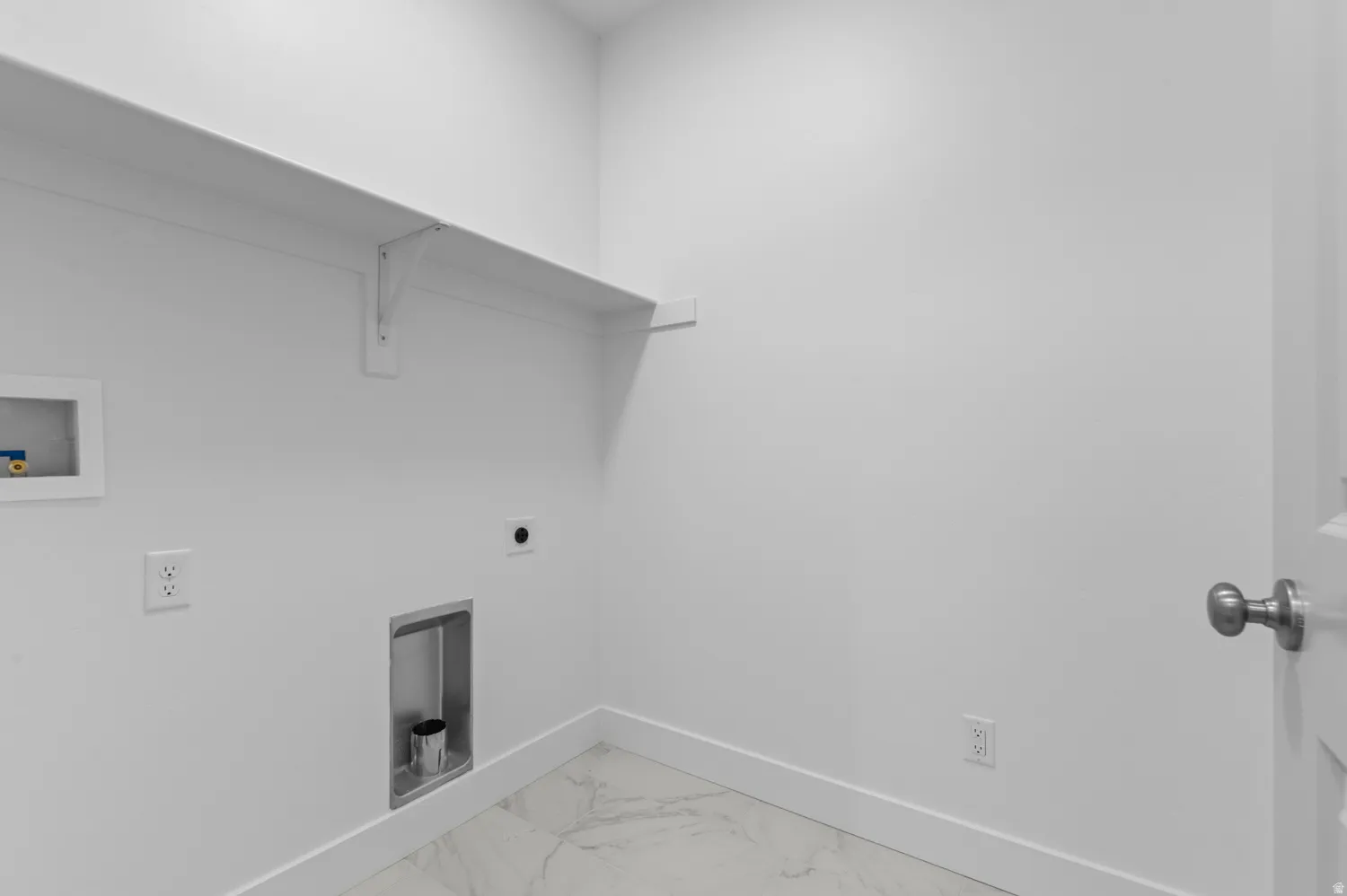 Dedicated laundry area featuring a white storage shelf, white walls, and a white door with a brushed nickel knob