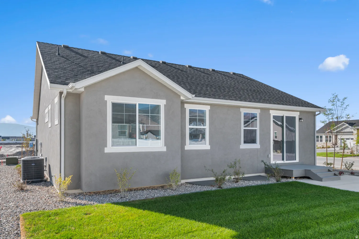 Exterior featuring gray stucco siding, a dark shingle roof, white trim windows, and a sliding glass door leading to a wooden deck