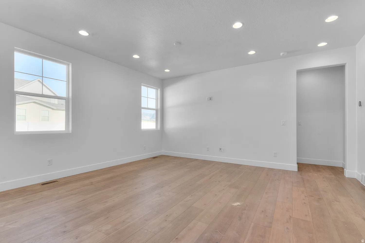 Spacious room featuring wood-finish flooring, recessed lighting, and bright white walls