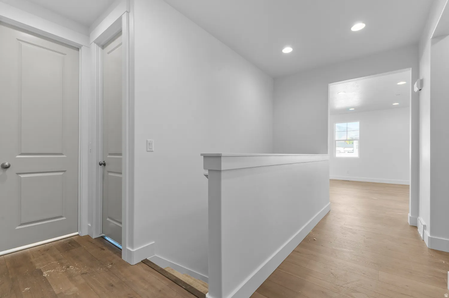 Upper-level hallway featuring wood-finish flooring, recessed lighting, crisp white walls, and a contemporary half-wall railing