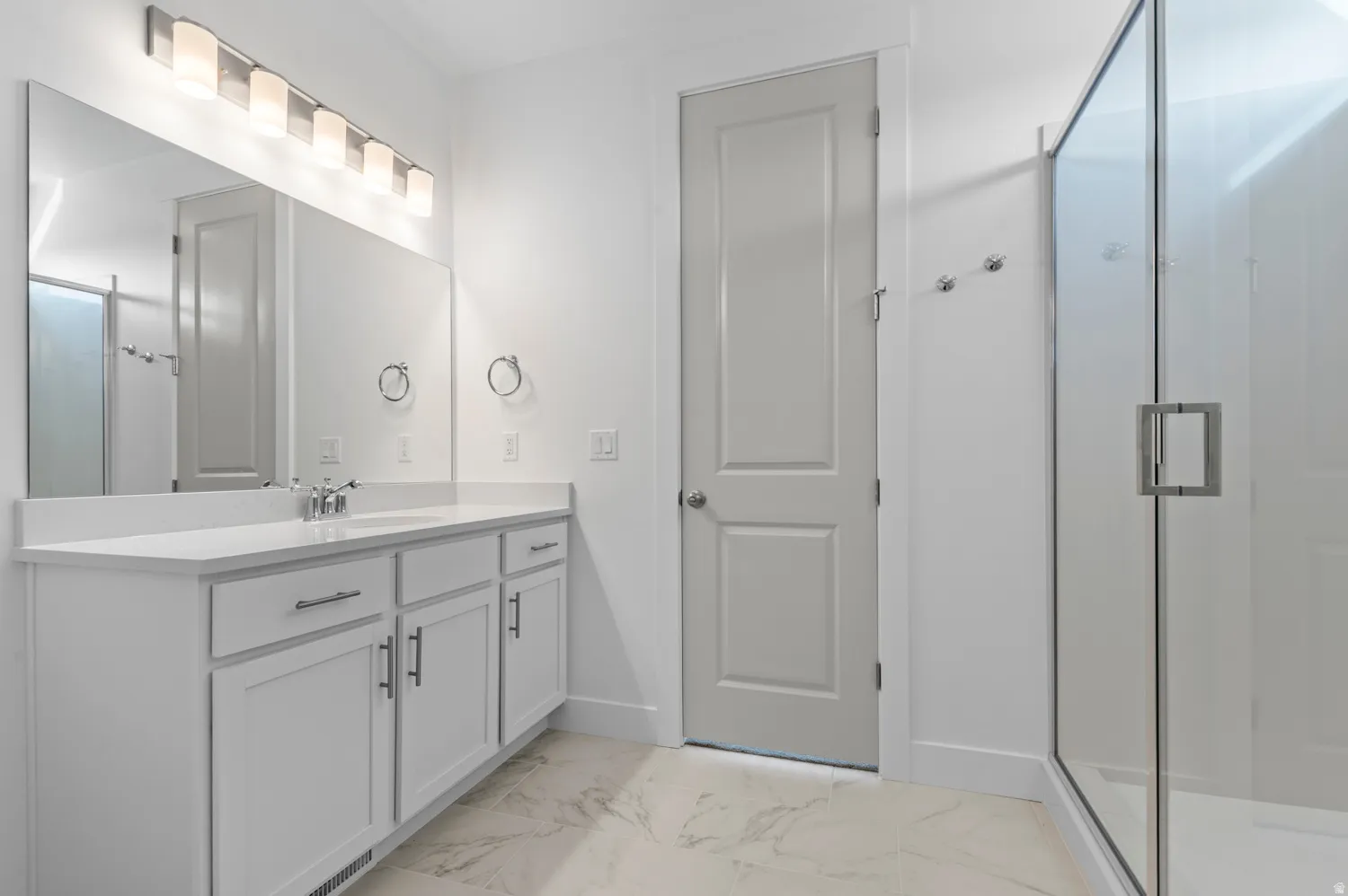Spacious bathroom featuring a double vanity with white cabinetry, a large vanity mirror, and a glass-enclosed shower