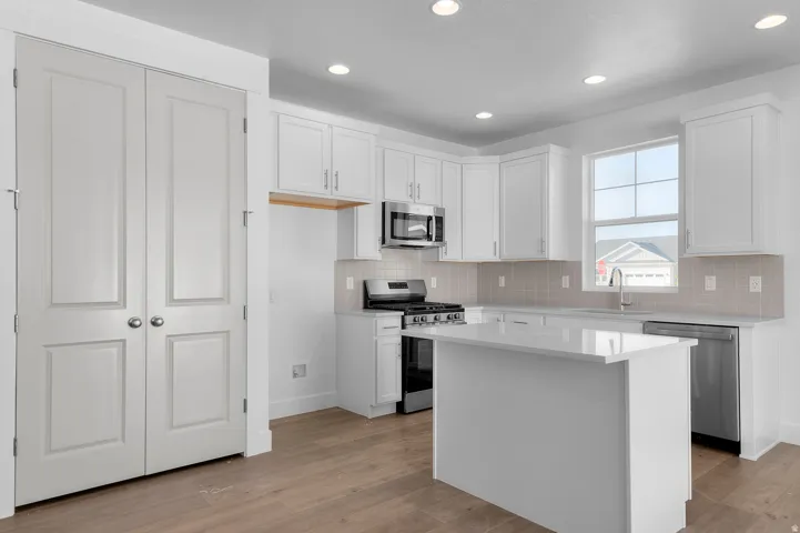 Modern kitchen featuring white cabinetry, a central island with a solid surface countertop, stainless steel appliances, and wood-finish flooring