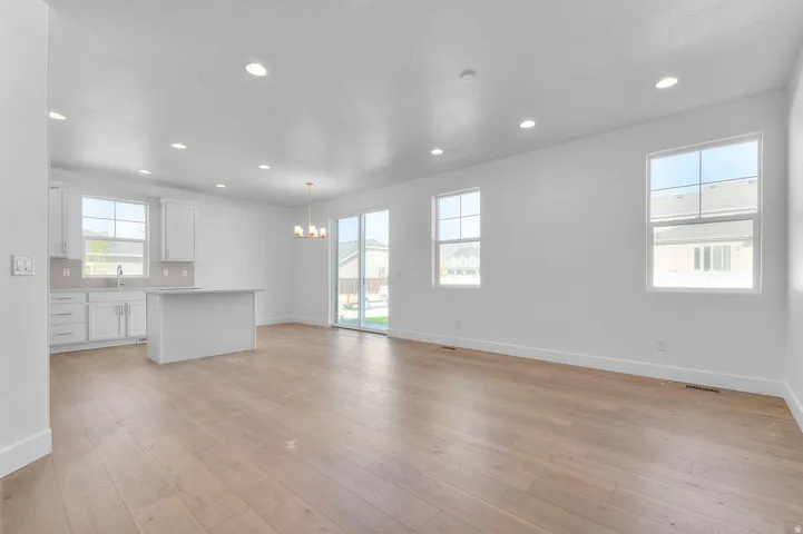 Open-concept living space featuring wood-finish flooring, recessed lighting, and ample natural light from multiple windows and a sliding glass door