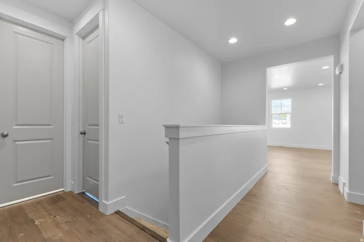 Upper-level hallway featuring wood-finish flooring, recessed lighting, crisp white walls, and a contemporary half-wall railing