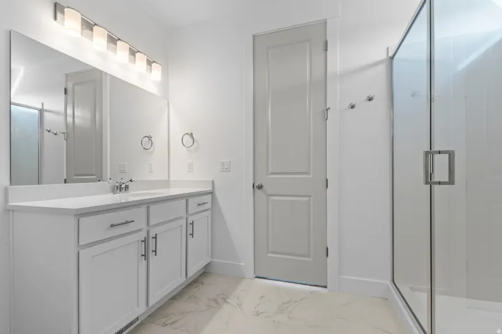 Spacious bathroom featuring a double vanity with white cabinetry, a large vanity mirror, and a glass-enclosed shower
