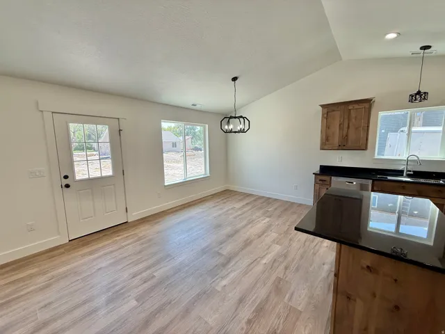 Bright and spacious open-concept kitchen and dining area featuring wood-finish flooring throughout, stainless steel appliances, dark countertops, natural wood cabinetry, and abundant natural light from multiple windows and glass door access to the exterio