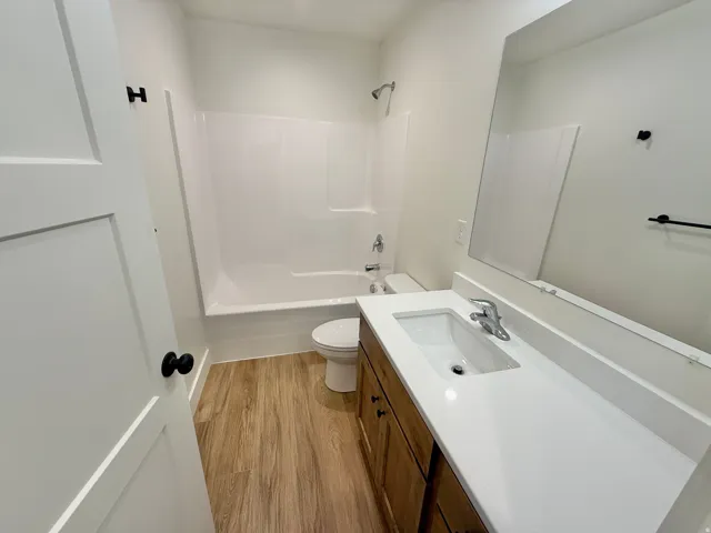 Modern bathroom featuring a wood-finish vanity with an undermount sink and white quartz countertop, matte black faucet and hardware, large framed mirror, and ceramic tile shower/tub combination with glass enclosure