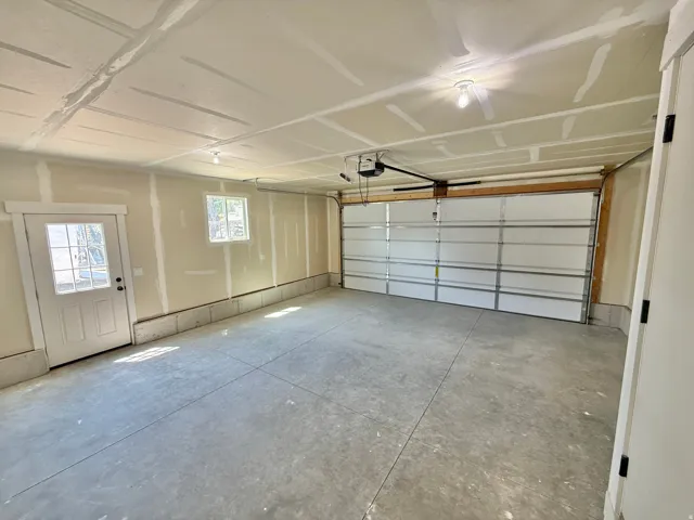 Spacious garage with a concrete floor, overhead garage door, and a paneled entry door with glass inserts