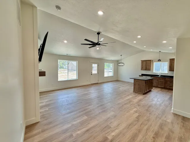 Open-concept living space featuring vaulted ceilings, recessed lighting, wood-finish flooring, a kitchen island, and a ceiling fan