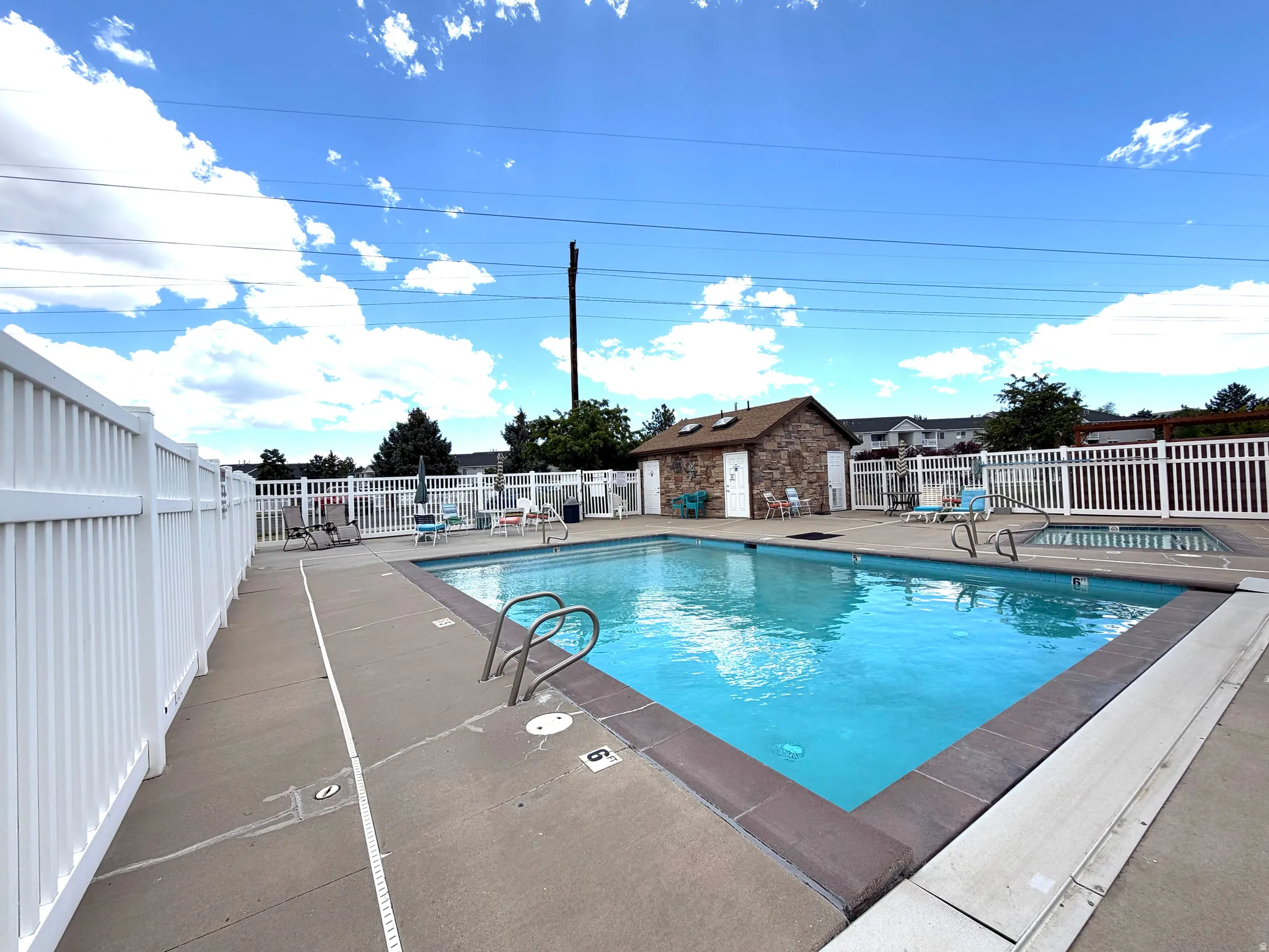 Community swimming pool featuring a concrete deck and white privacy fencing