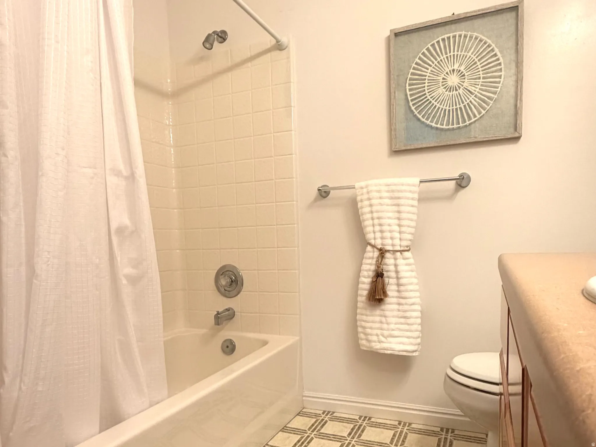 Bathroom featuring a white tub with ceramic tile surround, patterned floor tiling, and a vanity with a countertop and under-sink cabinetry