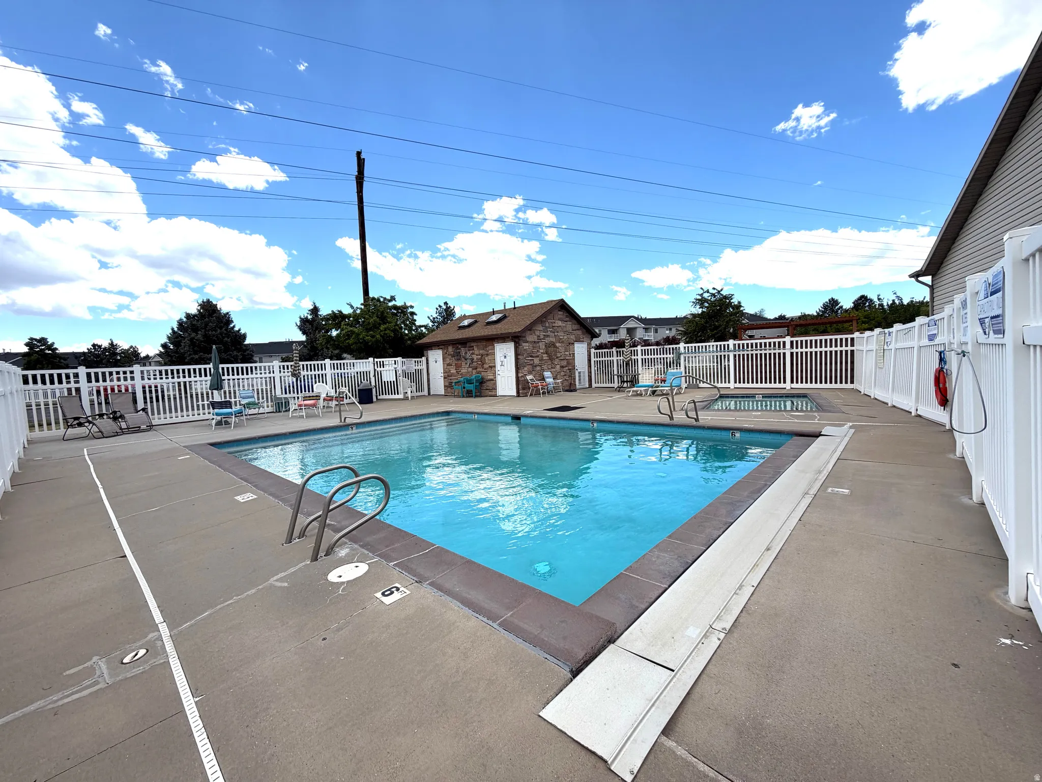 Community swimming pool featuring a concrete deck and white privacy fencing