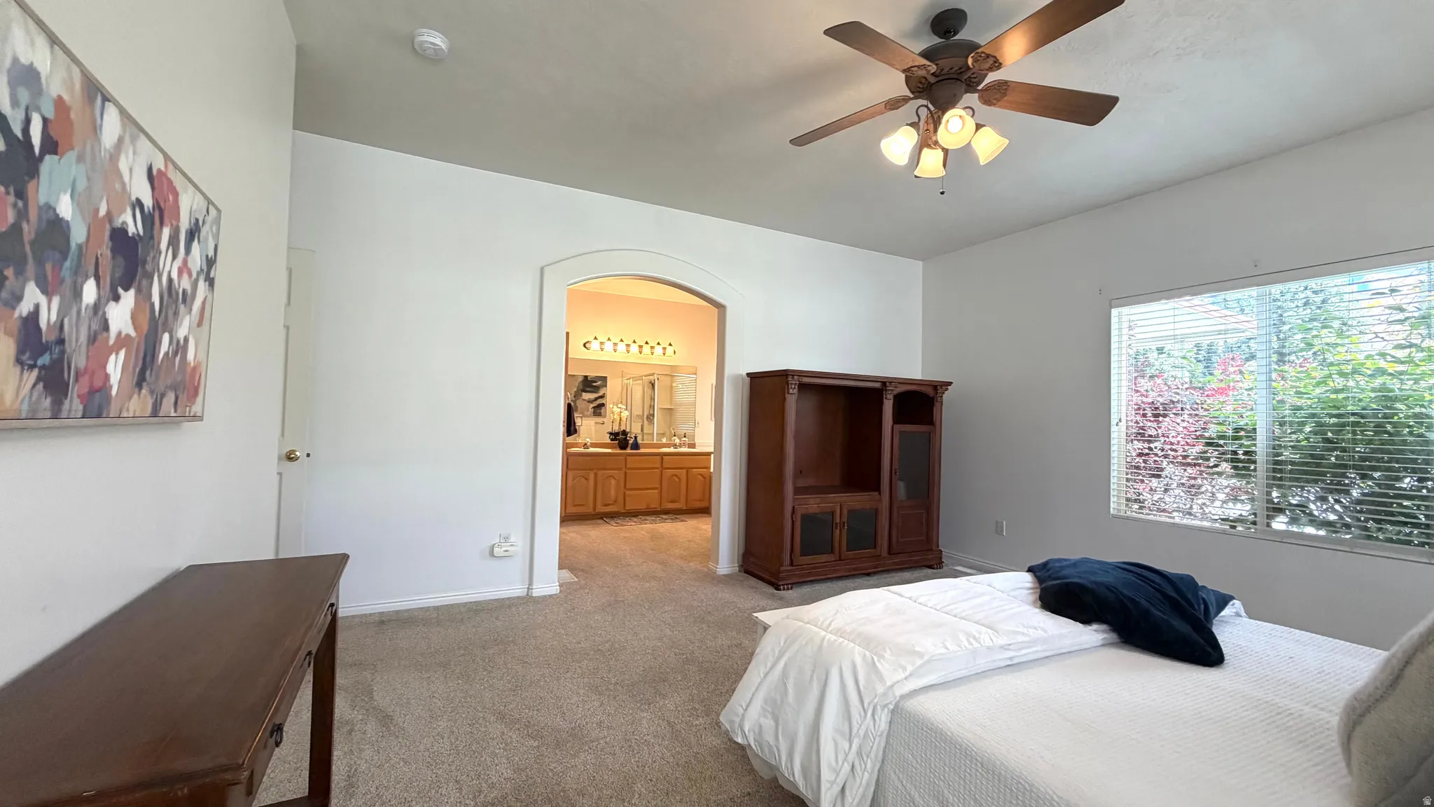 Carpeted interior space featuring an arched doorway, a ceiling fan with integrated lighting, and a window with horizontal blinds