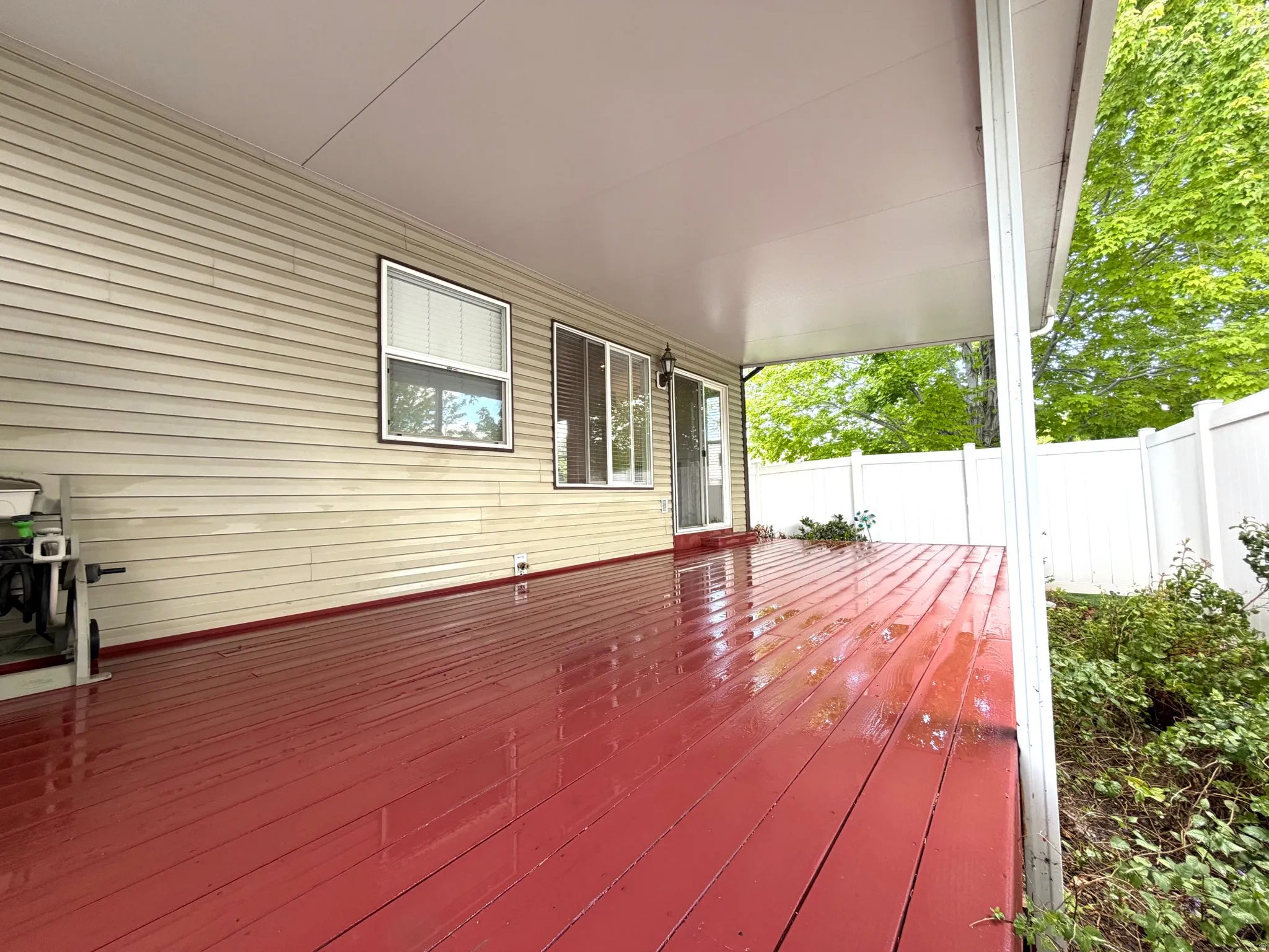 Covered deck featuring a red-stained wood surface, white vinyl siding, and a white privacy fence