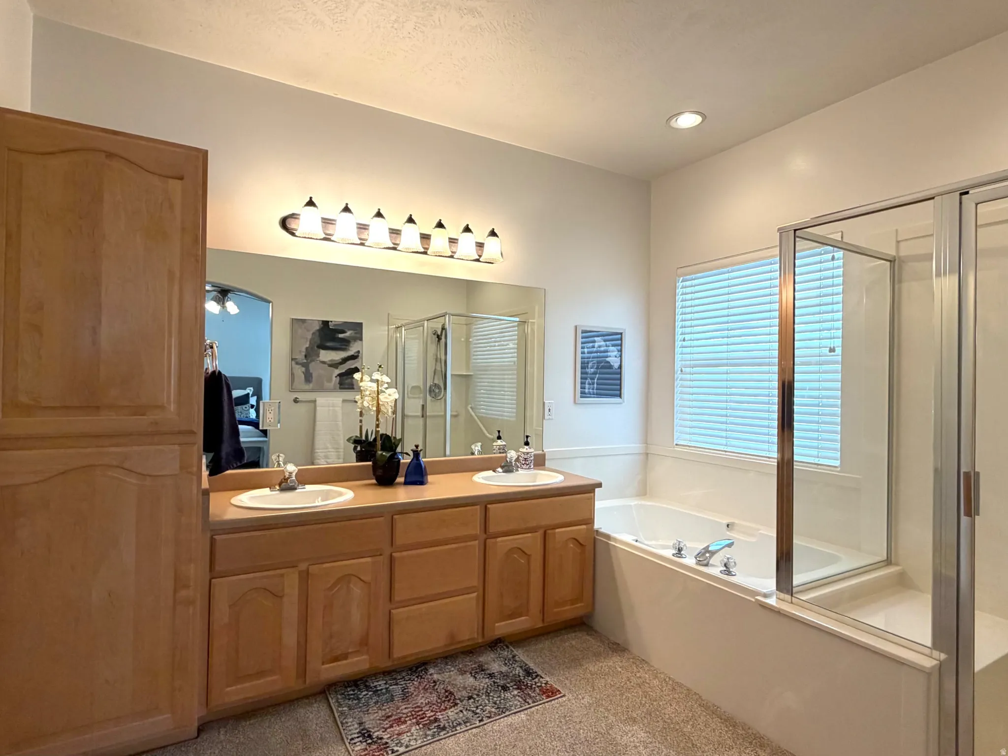 Bathroom featuring a double vanity with light wood cabinetry, dual sinks, and a long mirror