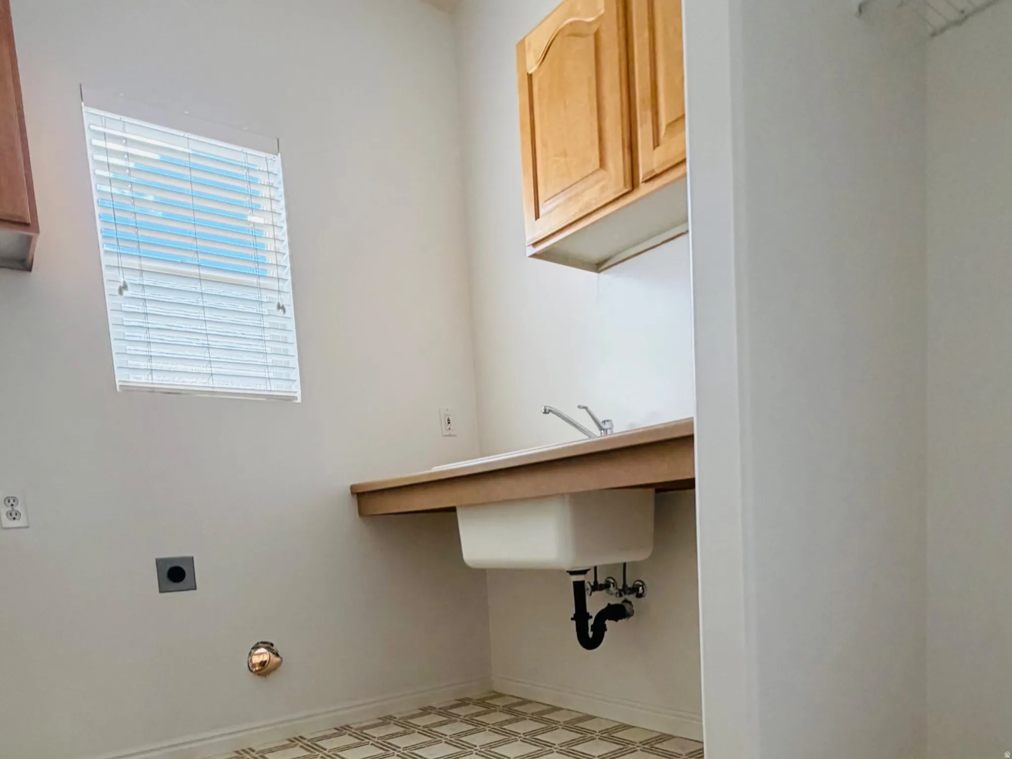Utility room featuring patterned flooring, a window with blinds, a utility sink with a base cabinet, and upper cabinetry